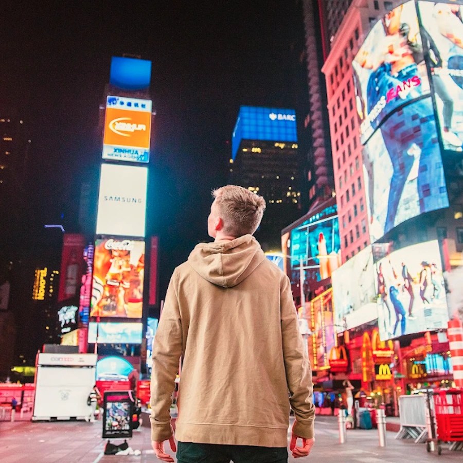 Person standing in a city center surrounded by bright digital billboards, representing digital out-of-home advertising.