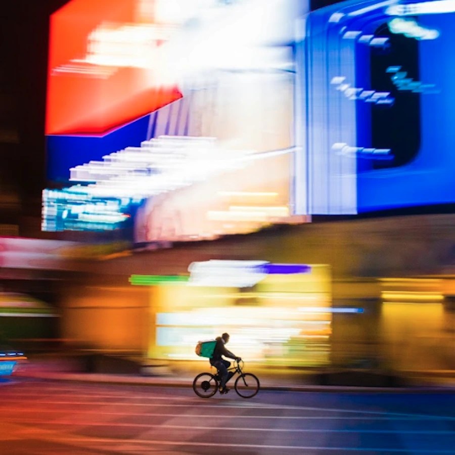 Cyclist riding past illuminated digital screens at night, symbolizing dynamic digital out-of-home advertising.