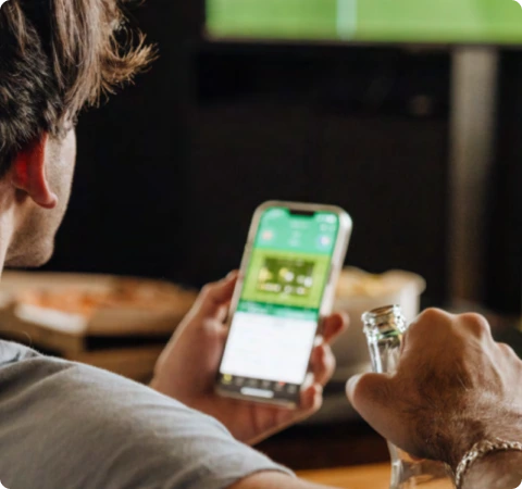 Man holding a phone and watching live sports streaming on a connected TV device